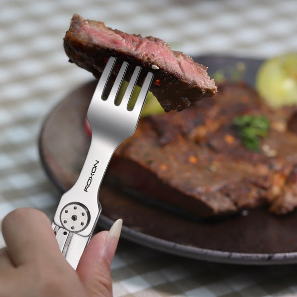 Fork with a piece of steak held above a plate of steak on a checkered tablecloth.
