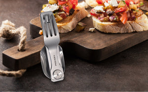 ROXON stainless steel foldable camping fork multitool placed on a dark wooden board with bruschetta in the background