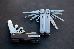 Two Roxon modular multitools on a dark surface, fully extended to show a variety of interchangeable blades and implements, including a knife, saw, scissors, hook, and file
