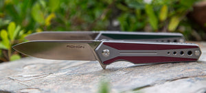 Folding knife with red handle and silver blade on a gray stone surface