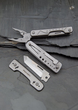 Roxon multitool with pliers partially open, shown next to an interchangeable tanto-style blade and tool cover, displayed on a textured stone surface.