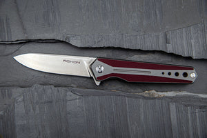 Folding knife with red and silver handle on a gray stone surface