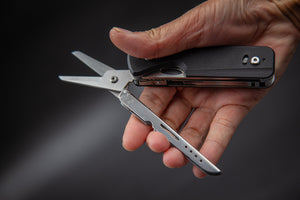 Multitool with scissors held in a hand against a dark background