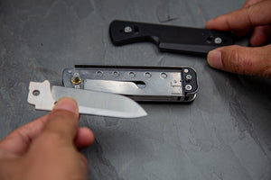 Close-up of a knife with a blade held by a hand on a gray surface