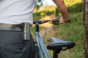 Person standing next to a bicycle on a forest trail with a Roxon multitool clipped to their belt, showcasing its portability and everyday carry convenience.