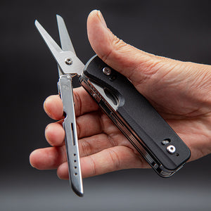 Multitool with scissors held in a hand against a dark background
