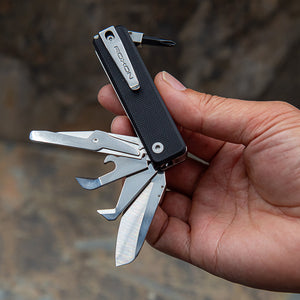 Multitool with various tools held in a hand against a blurred natural background