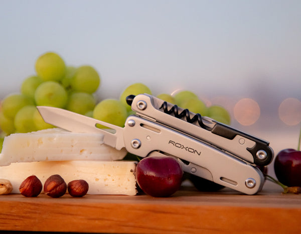 Storm multitool with the blade cutting through cheese on a platter that has grapes and nuts and cherries.