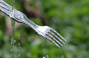 Metallic fork with water droplets against a blurred green background