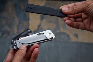 Two folding knives held by hands against a blurred background
