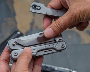 Close-up of hands holding a multi-tool with additional tools on a reflective surface