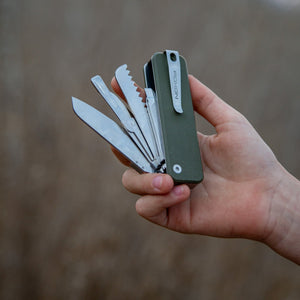 Hand holding a multi-tool with various blades against a blurred background