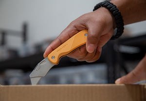 Hand holding a knife with an orange handle, blurred background