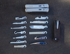Top-down view of two Roxon modular multitool frames laid out on a dark surface, surrounded by a variety of interchangeable implements including blades, files, saws, openers, and specialty tools.