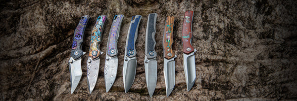 Row of folding knives with decorative handles on a textured dark background
