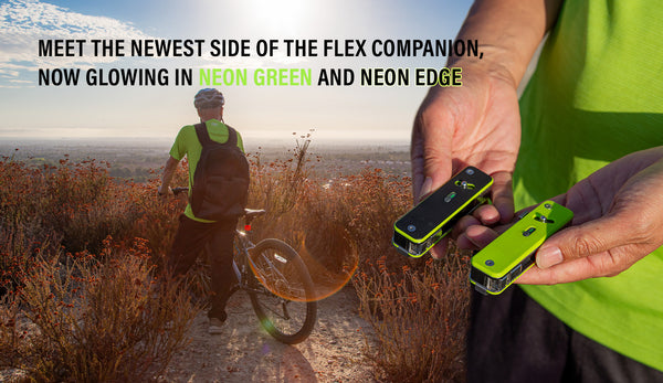 Person holding glowing green and neon edge multi tools with a person on a bike in the background.