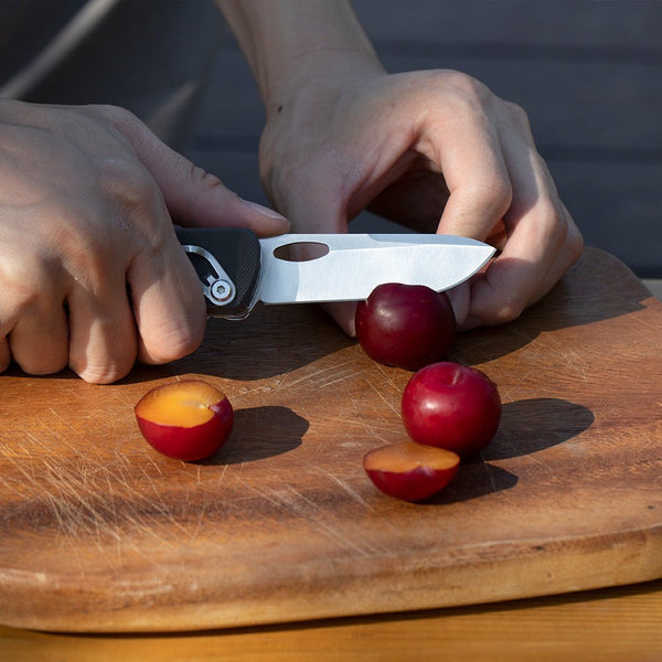Person cutting plums on a wooden cutting board with a knife.