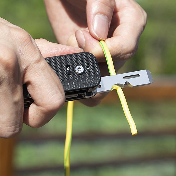 Person using a tool to strip the insulation off yellow electrical wire with a blurred green background