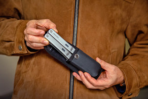 Person holding a black folding knife against a brown leather jacket background