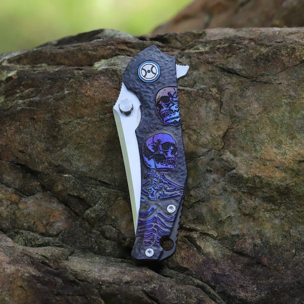 Folding knife with skull design on a rock