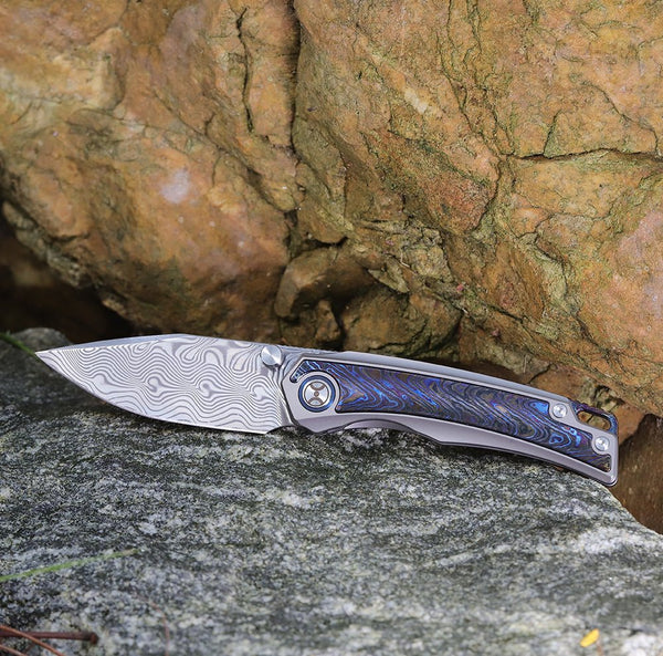 Folding knife with a decorative blade and handle on a rocky surface
