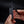 Person holding a small black device with a pair of scissors attached on a dark background