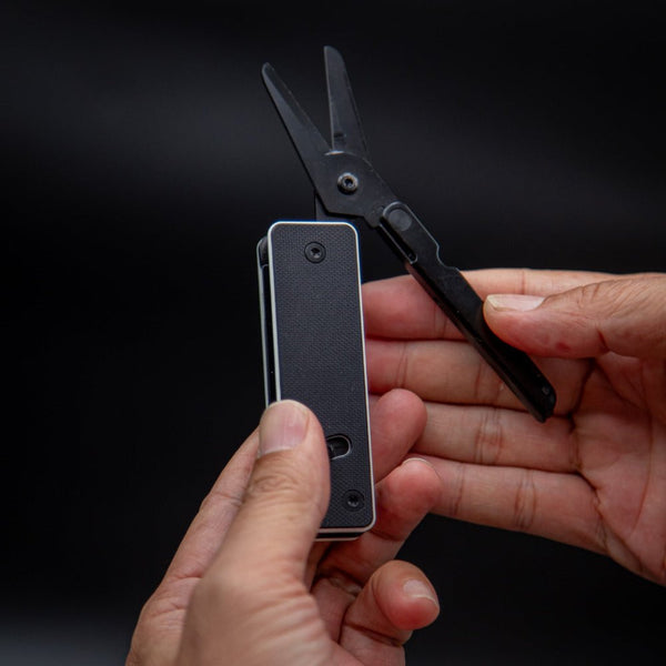 Person holding a small black device with a pair of scissors attached on a dark background