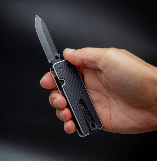 Hand holding a black folding knife against a dark background