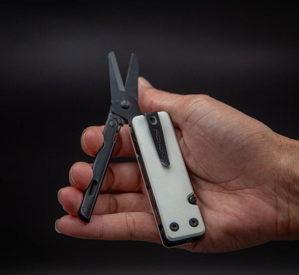 Hand holding a multi-tool with scissors on a black background