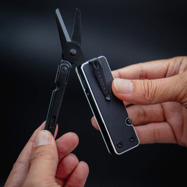 Multitool with shears held by hands against a dark background